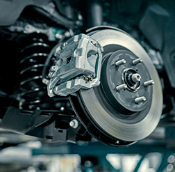 A close-up view of a brake rotor and brake pad on a lifted vehicle in a service center.