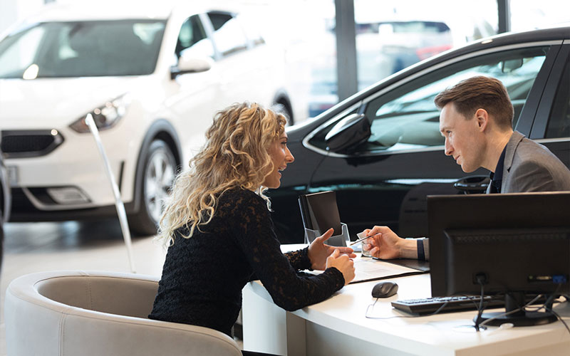 Salesperson speaking with a customer at their desk in the dealership