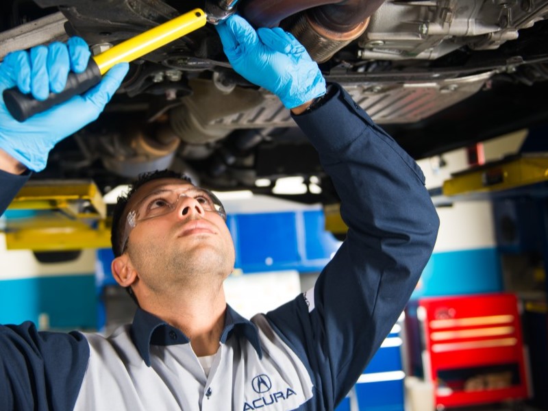 An Acura Service Technician performing maintenace under an vehicle in the service center.