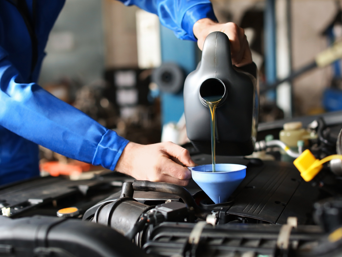 Close-up of a service technician replenishing the oil of a vehicle in the service center.
