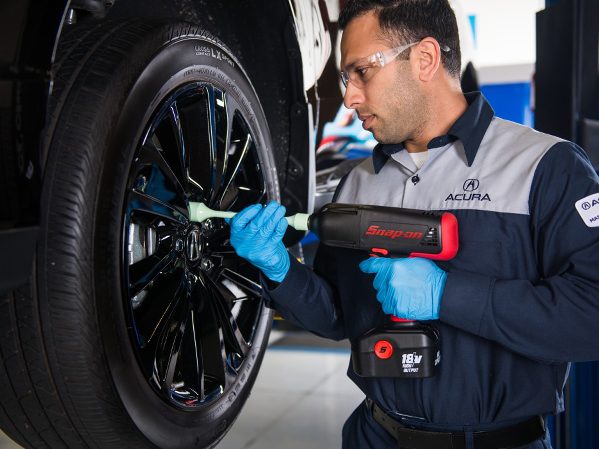 A Acura Service Technician performing service on a vehicle's wheel in the service center.