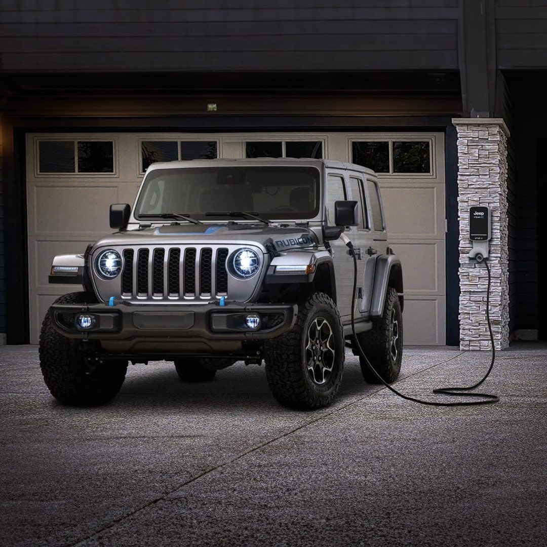 A Jeep 4xe parked at home and plugged into a home charging station in front of the garage