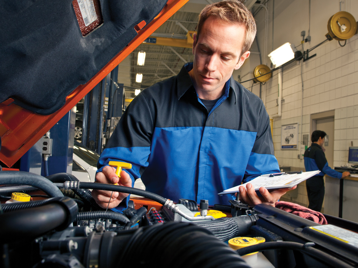 A service technician performing a routine multi-point vehicle inspection and checking fluid levels under the hood of a car.