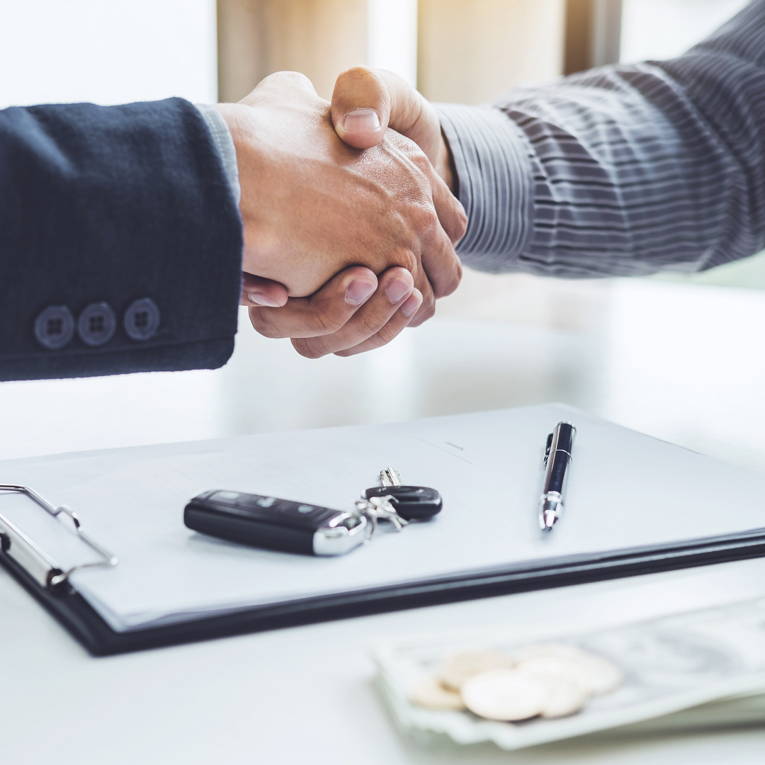 2 people shaking hands over a finance application and car key fob.