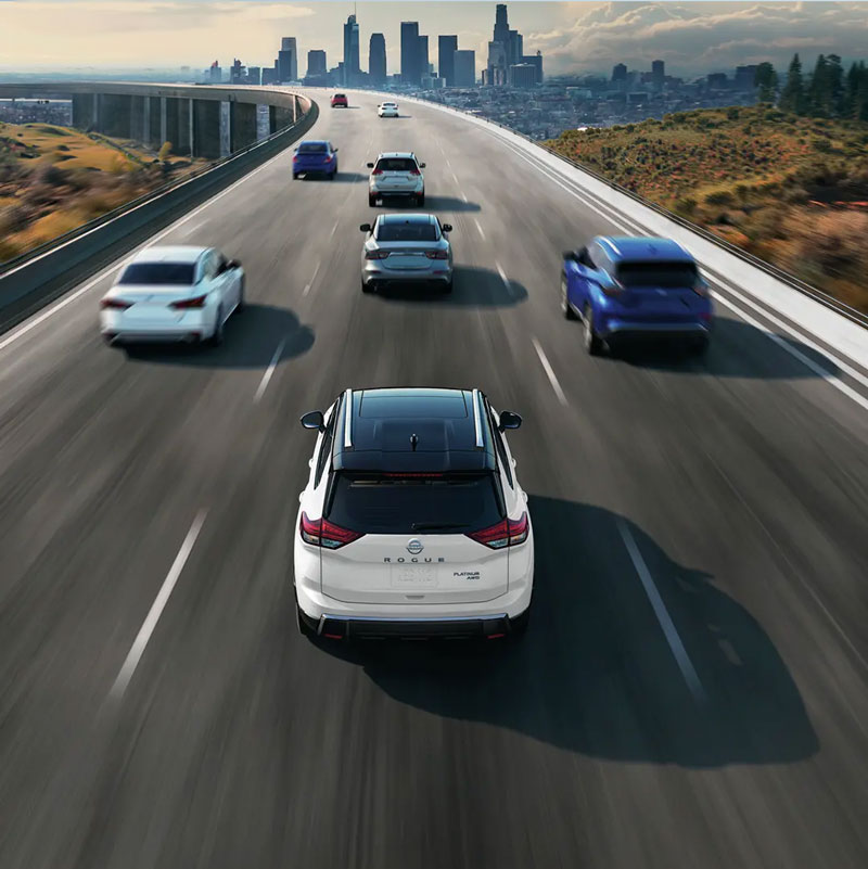 Nissan Rogue driving towards a city on the highway near multiple other Nissan vehicles.