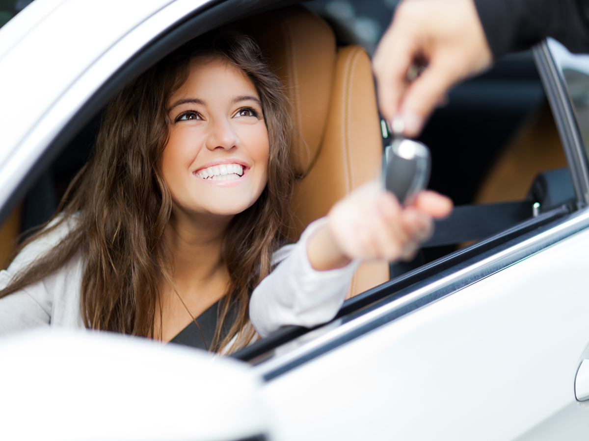 A smiling driver sitting in a car holding out their hands for the car keys.