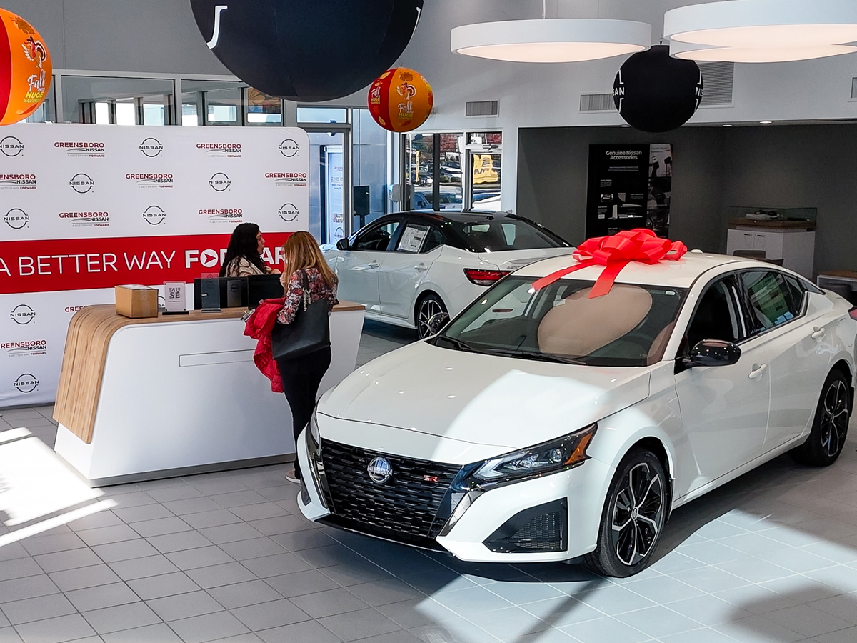 Inside the Greensboro Nissan dealership showroom with multiple Nissan models on display.