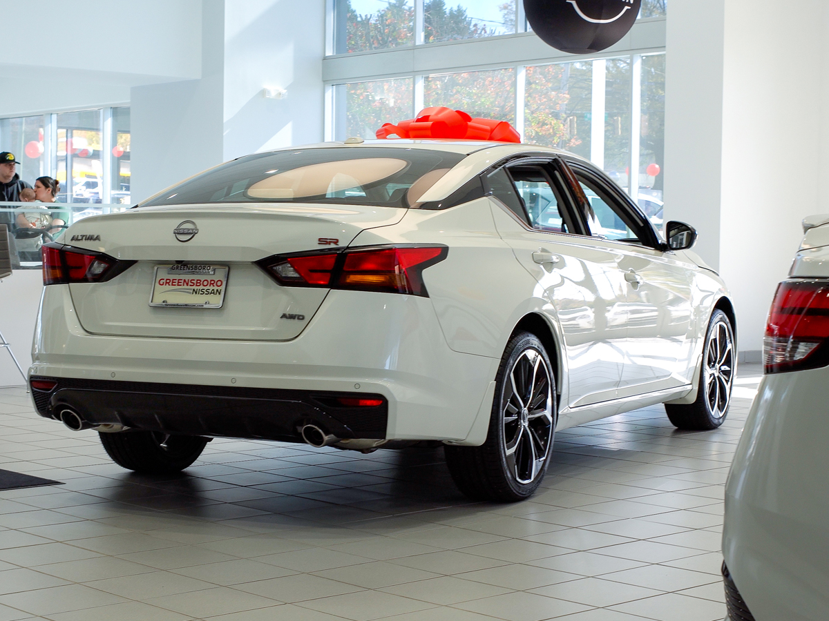 A white Nissan Altima with a red bow on top on display in the Greensboro Nissan dealership showroom.