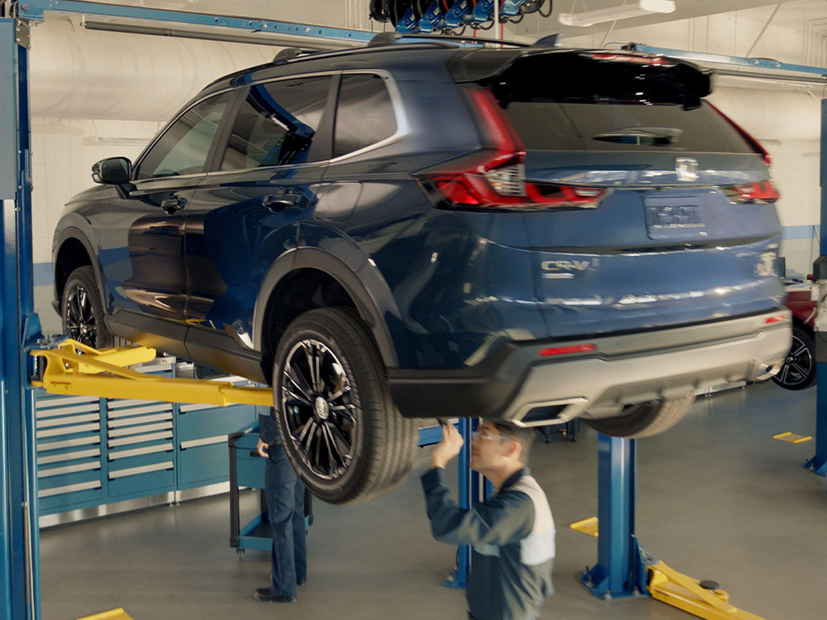 A Service Technician under a vehicle in the service center on a lift.