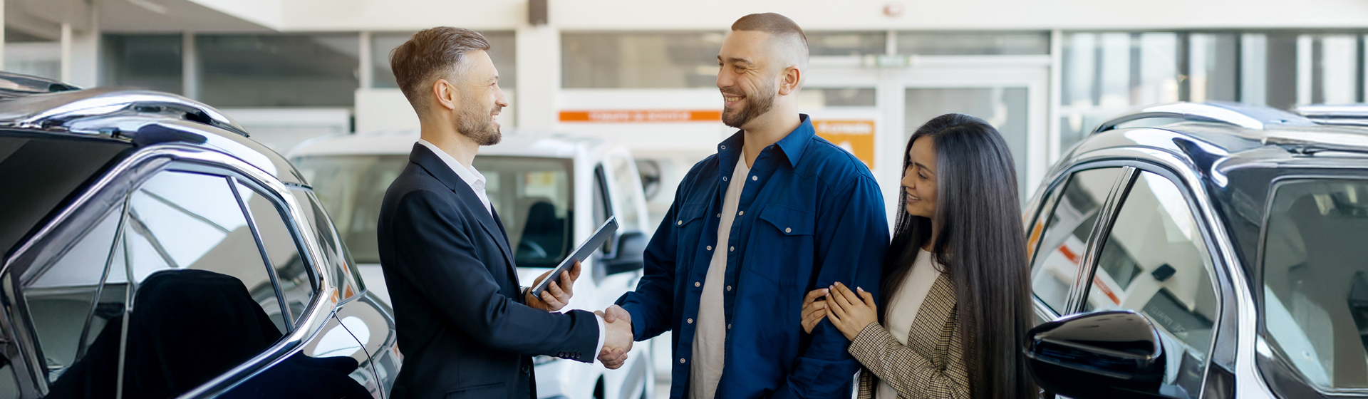 A car salesperson shaking hands with a happy couple in the car dealership.