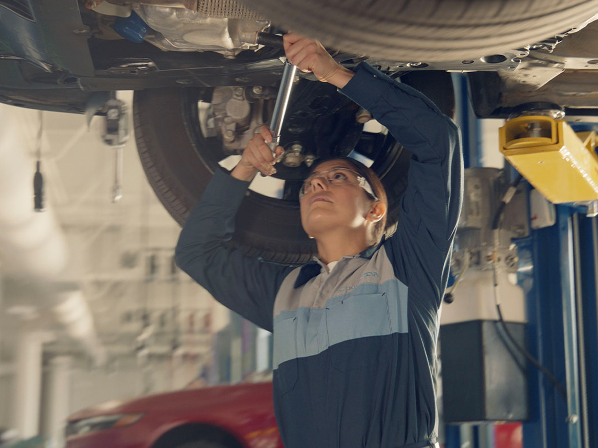 A Service Technician under a vehicle in the service center on a lift.