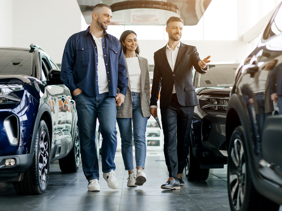 A car salesperson showing vehicles to a couple in the car dealership.