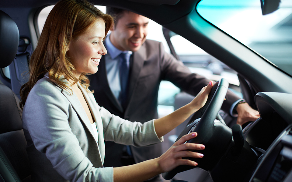 A salesperson showing off the interior of a car while the customer sits happily inside