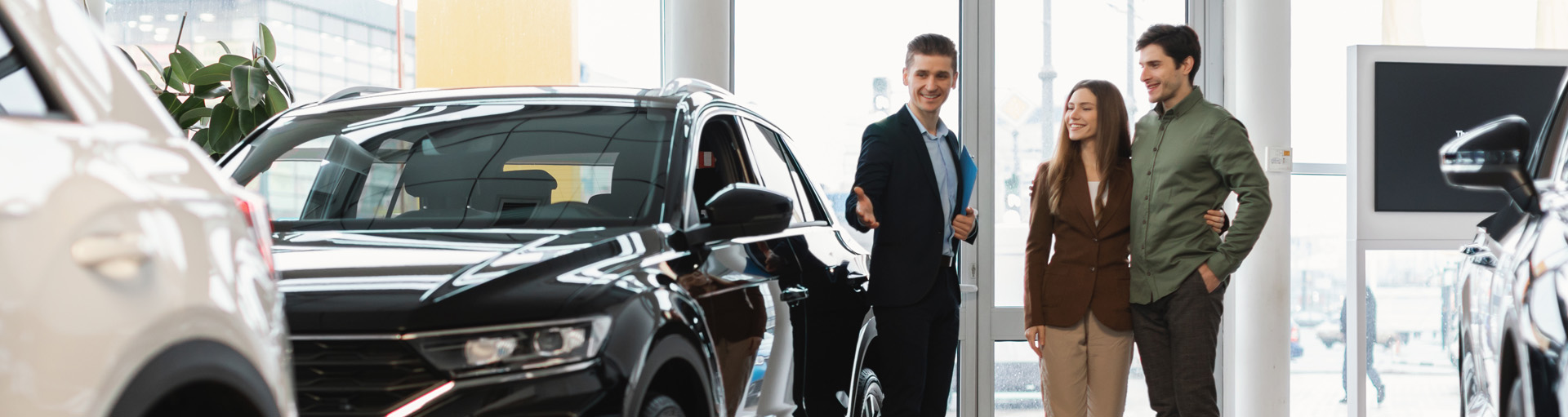 A car salesperson showing off vehicles in the car dealership to a couple