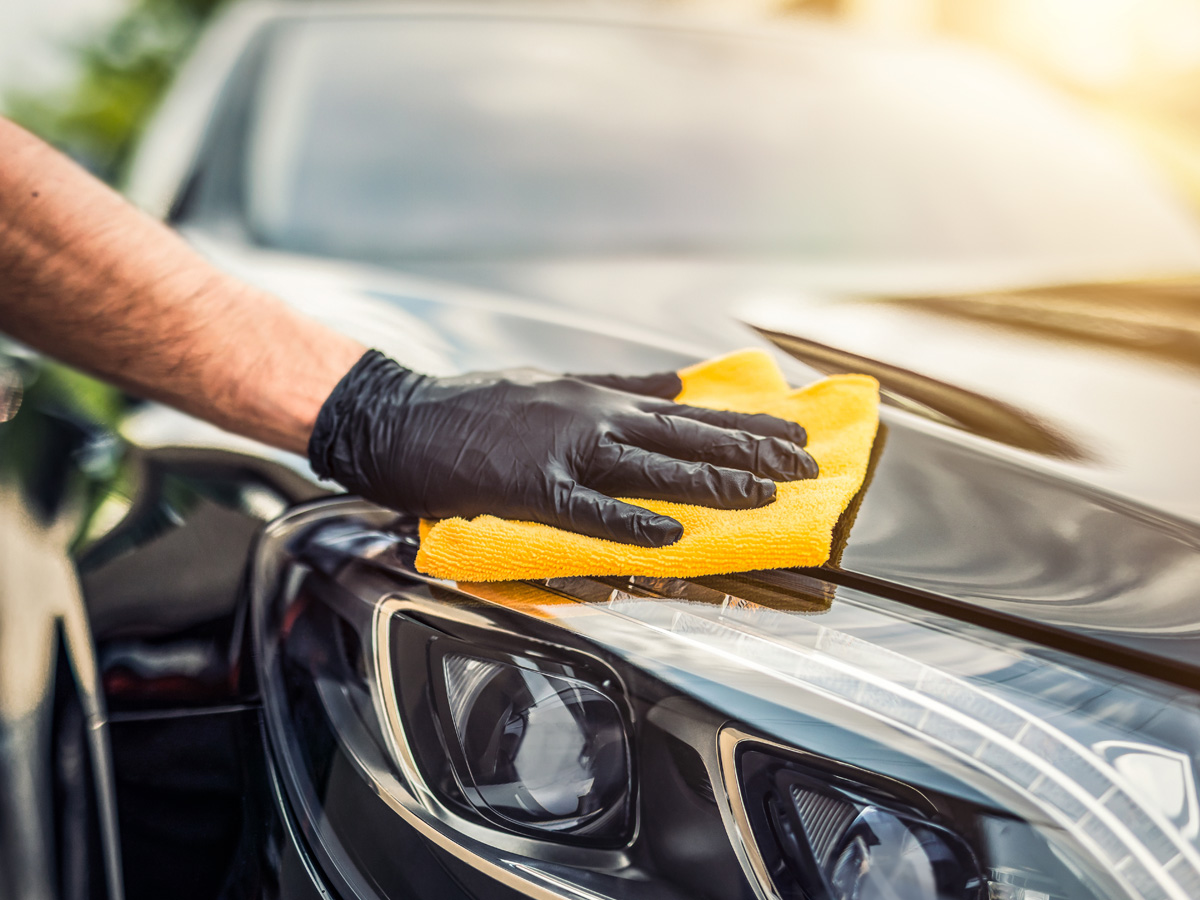 A close-up of someone's hand holding a microfiber towel wiping a car clean