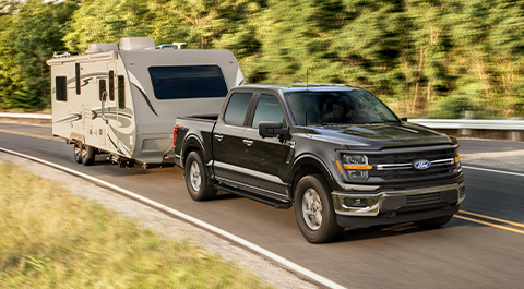A black Ford F-150 pickup truck driving on a road pulling a trailer.