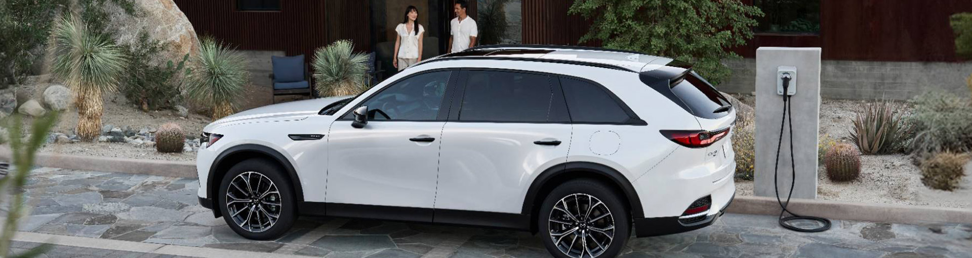 Mazda CX-70 parked in front of a family's home by an EV charging station