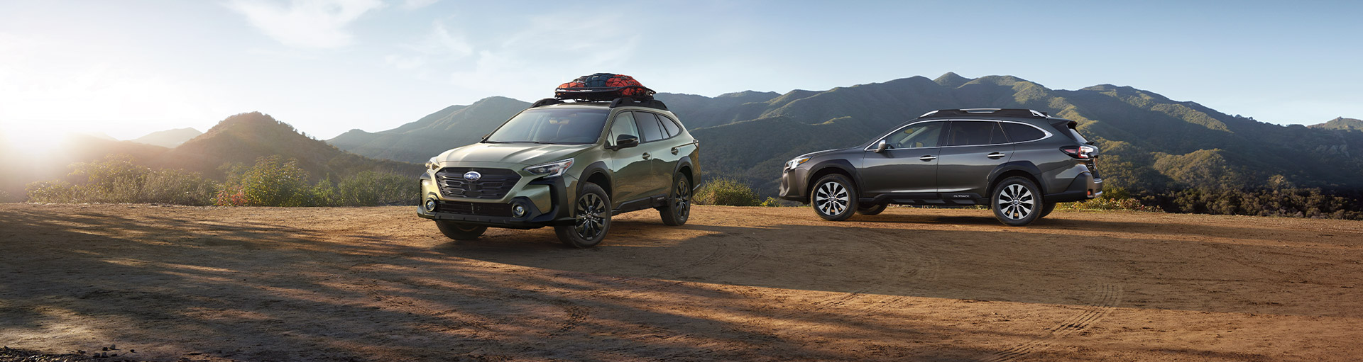 Two Subaru Outbacks parked in different angles off-road with a mountain view