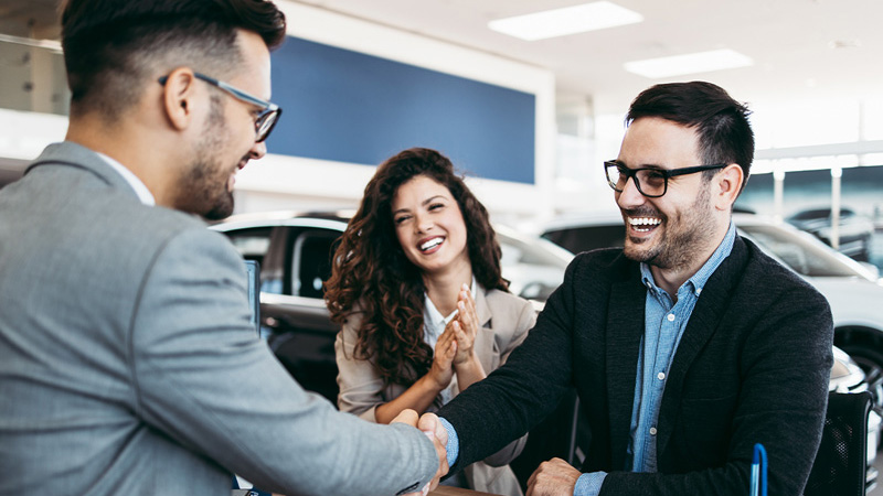 A happy couple shaking hands with a car salepersons in the car dealership