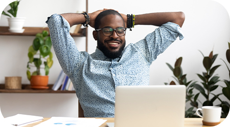 A man with his hands on his head and smiling while looking at his computer