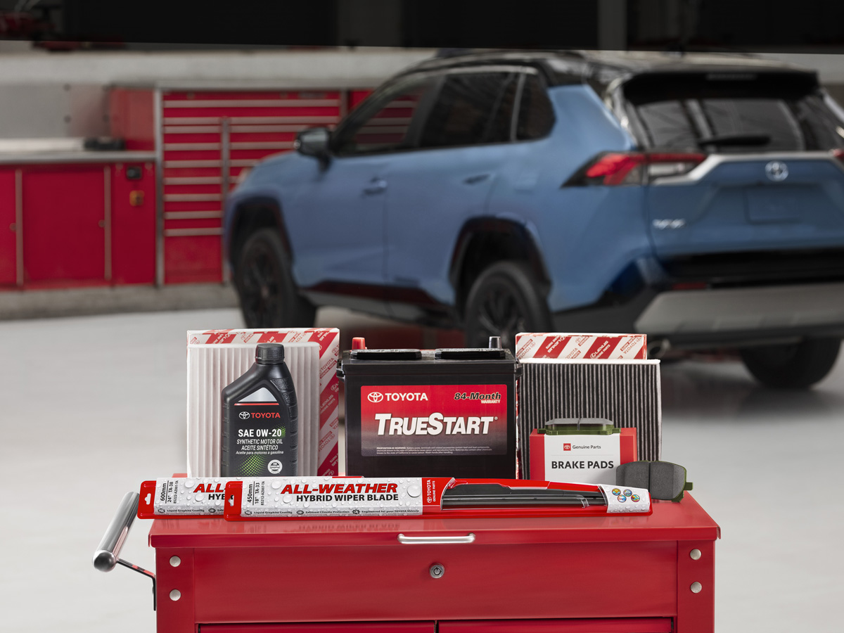Genuine Toyota parts and maintenance products displayed on a red rolling tool cabinet in front of a parked Toyota RAV4 in a service center.