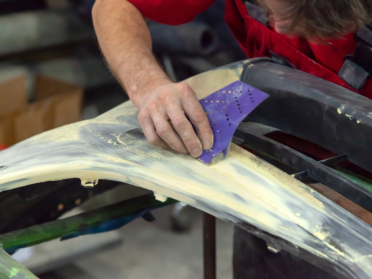 A service technician sanding down the panel of a car.