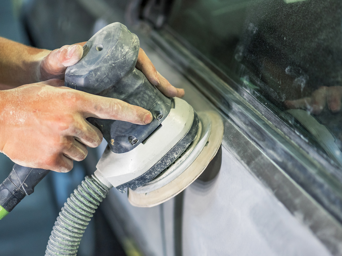 A service technician using a tool to sand down the panel of a car.