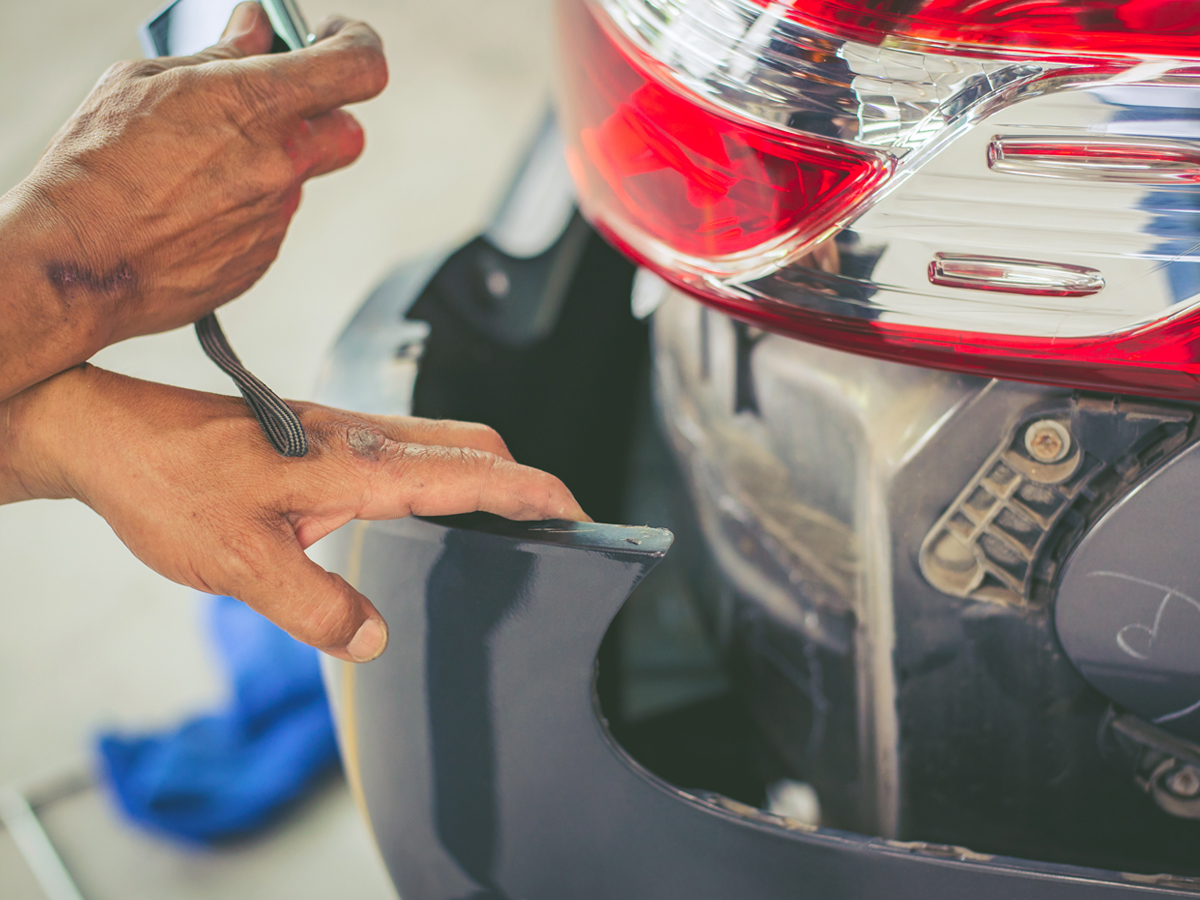 A service technician measuring the back bumper of a vehicle.