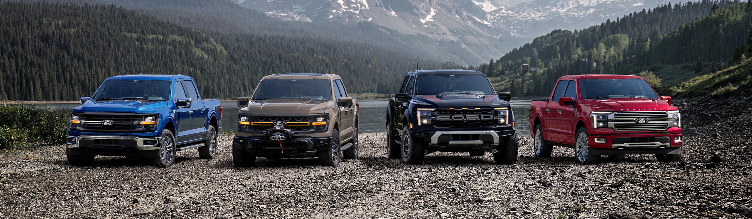A line-up of Ford truck models parked off-road by a lake