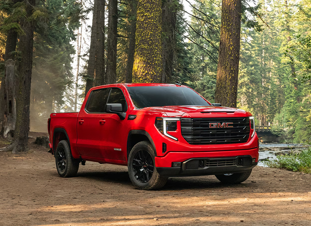 A red GMC Sierra 1500 Elevation pickup truck parked on a dirt path in a forest.
