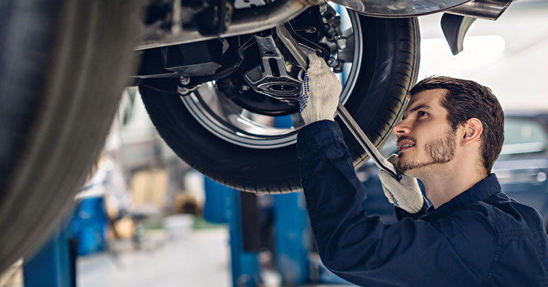 A Hyundai service technician performing vehicle service under a car