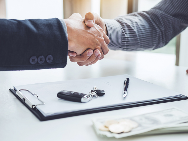 A salesperson and client shaking hands over their new car keys and paperwork