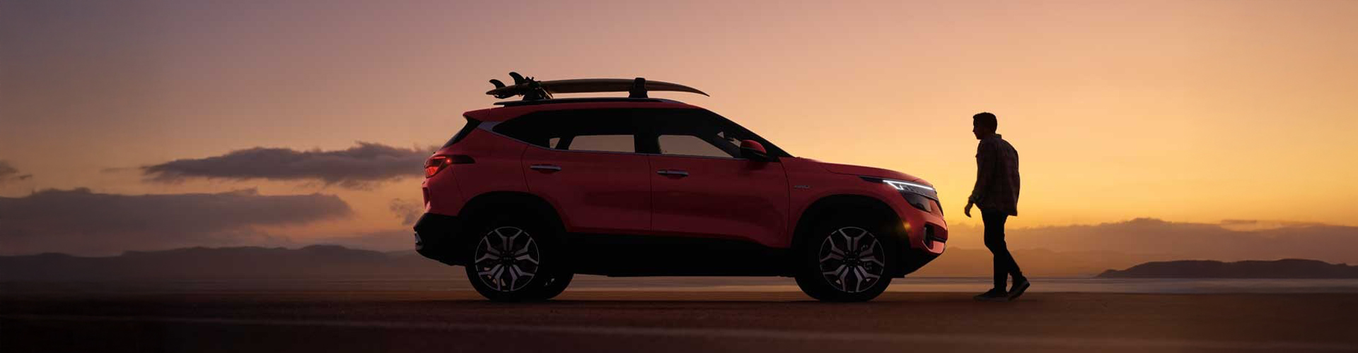 A Kia Seltos with a accessory rack on top parked on the beach at sunset
