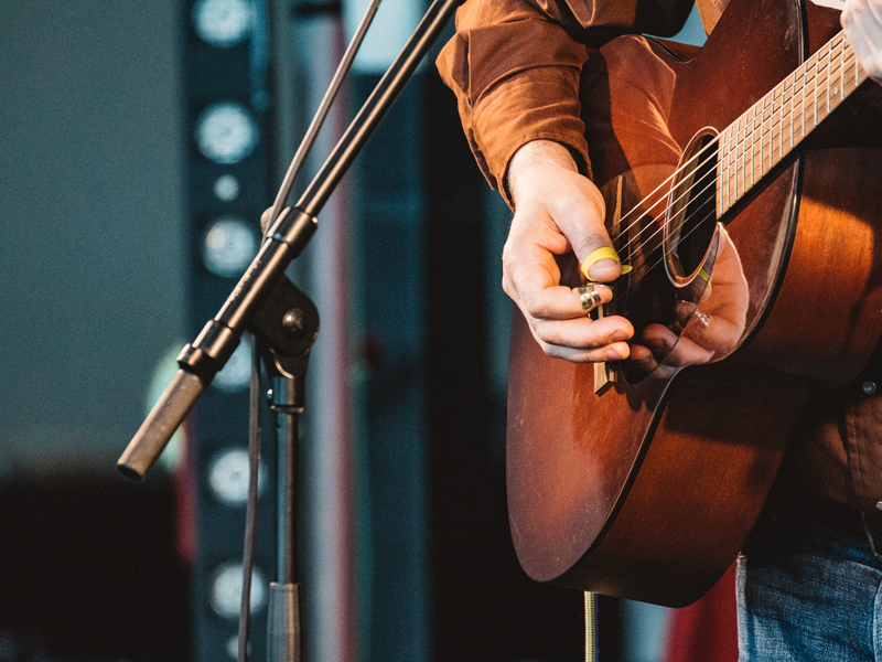 A close-up of someone's hands strumming a guitar in front of a microphone
