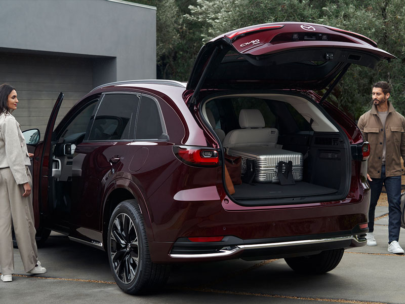 A couple packing up their Mazda CX-90 in front of a garage