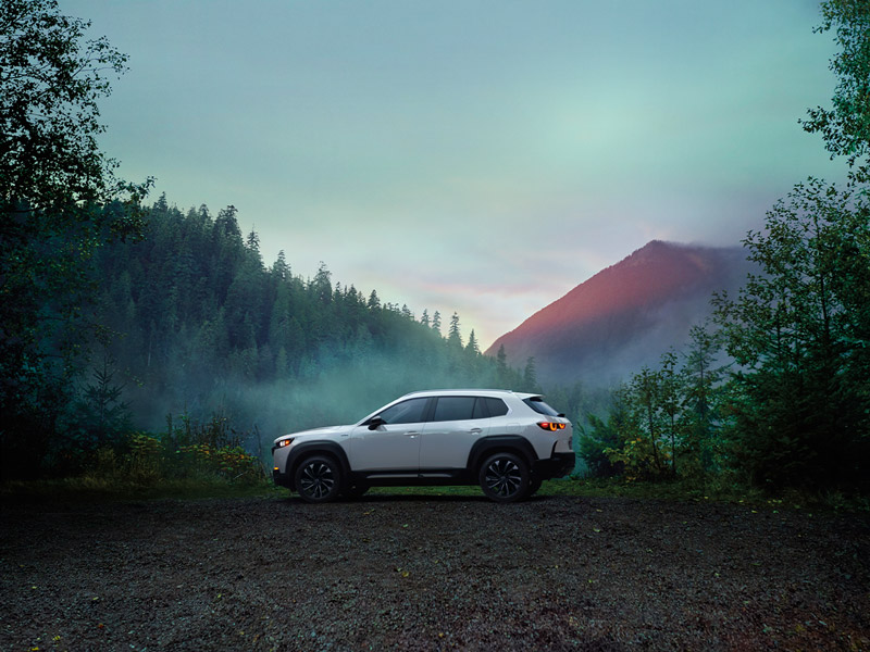 A white Mazda SUV model parked off-road in a foggy forest