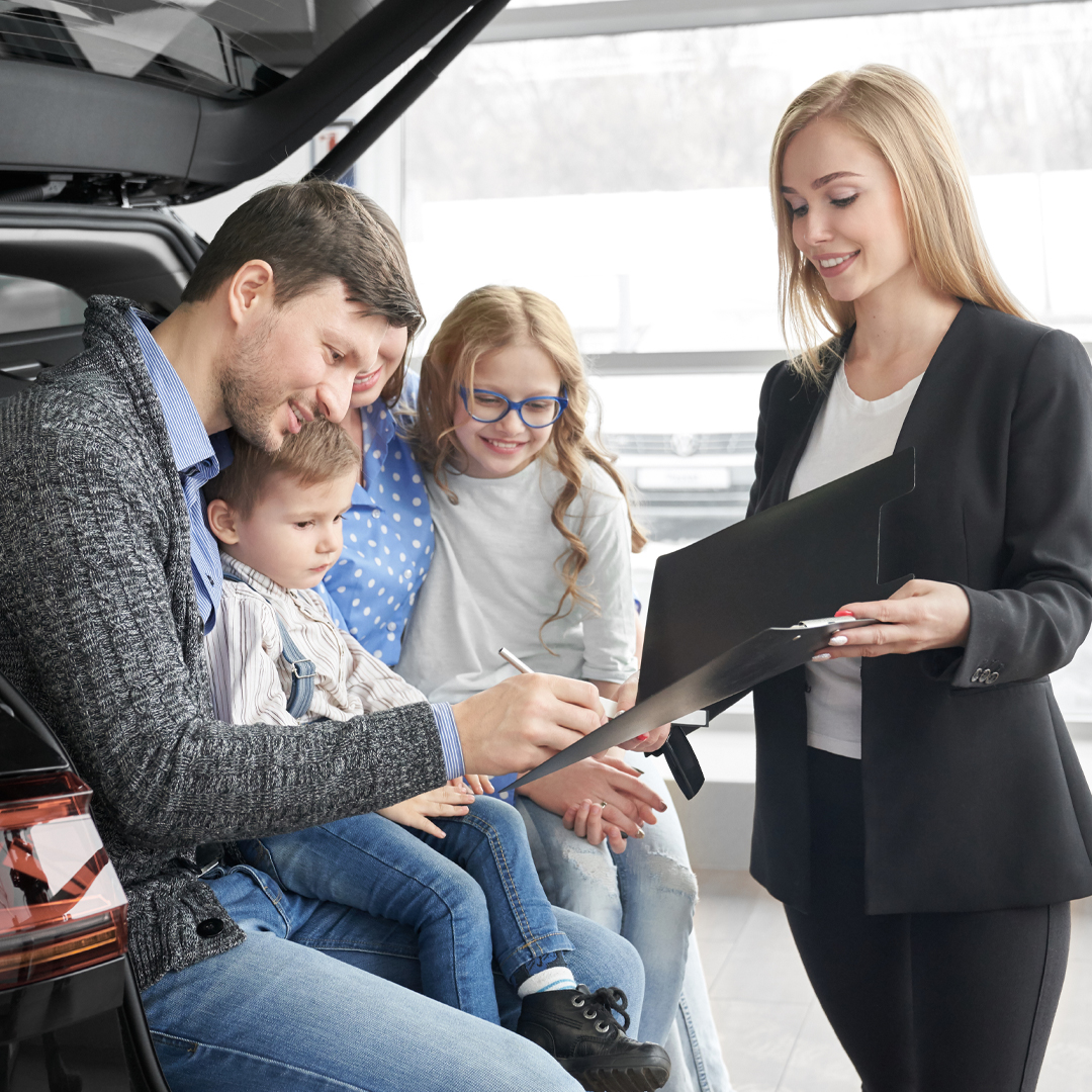 A family sitting in a Mazda vehicle, signing paperwork for their new car