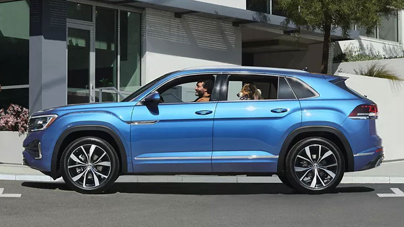 A man and his dog sitting in their Volkswagen Atlas parked in front of a building.
