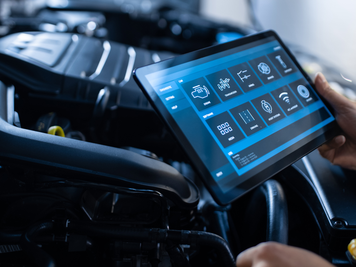 A service technician holding a tablet while performing a vehicle inspection.