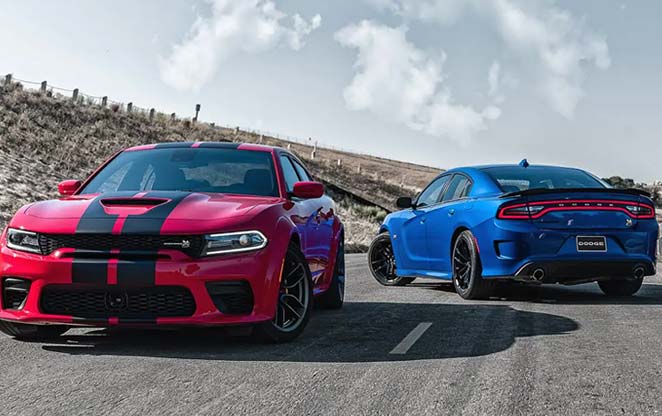 Photo of a red Dodge sports car with 2 black stripes and a blue Dodge sports car from behind both in the middle of a road